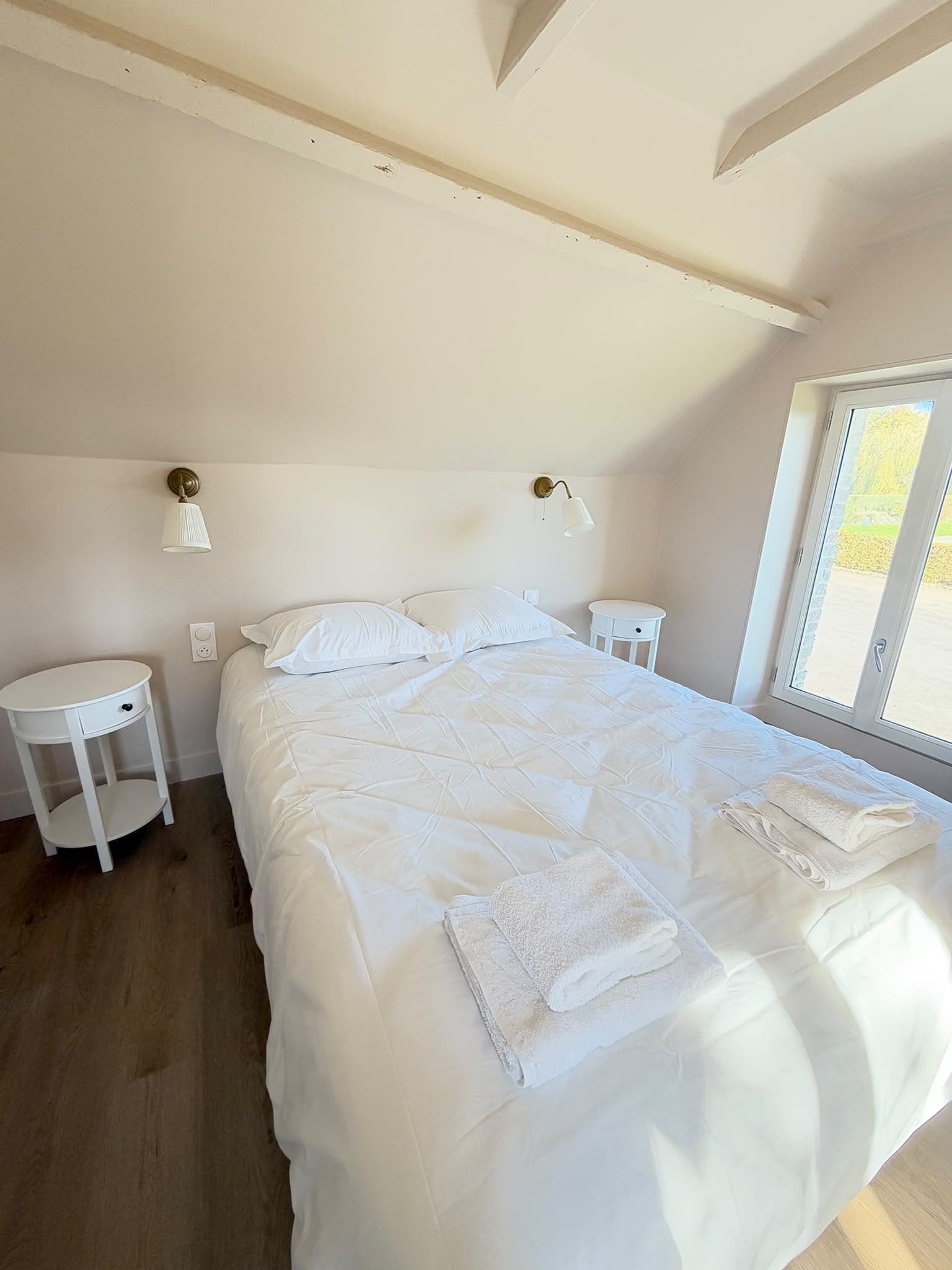 Een slaapkamer met een groot bed, twee nachtkastjes, een rond bijzettafeltje en een raam met uitzicht.