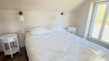 Een slaapkamer met een groot bed, twee nachtkastjes, een rond bijzettafeltje en een raam met uitzicht.