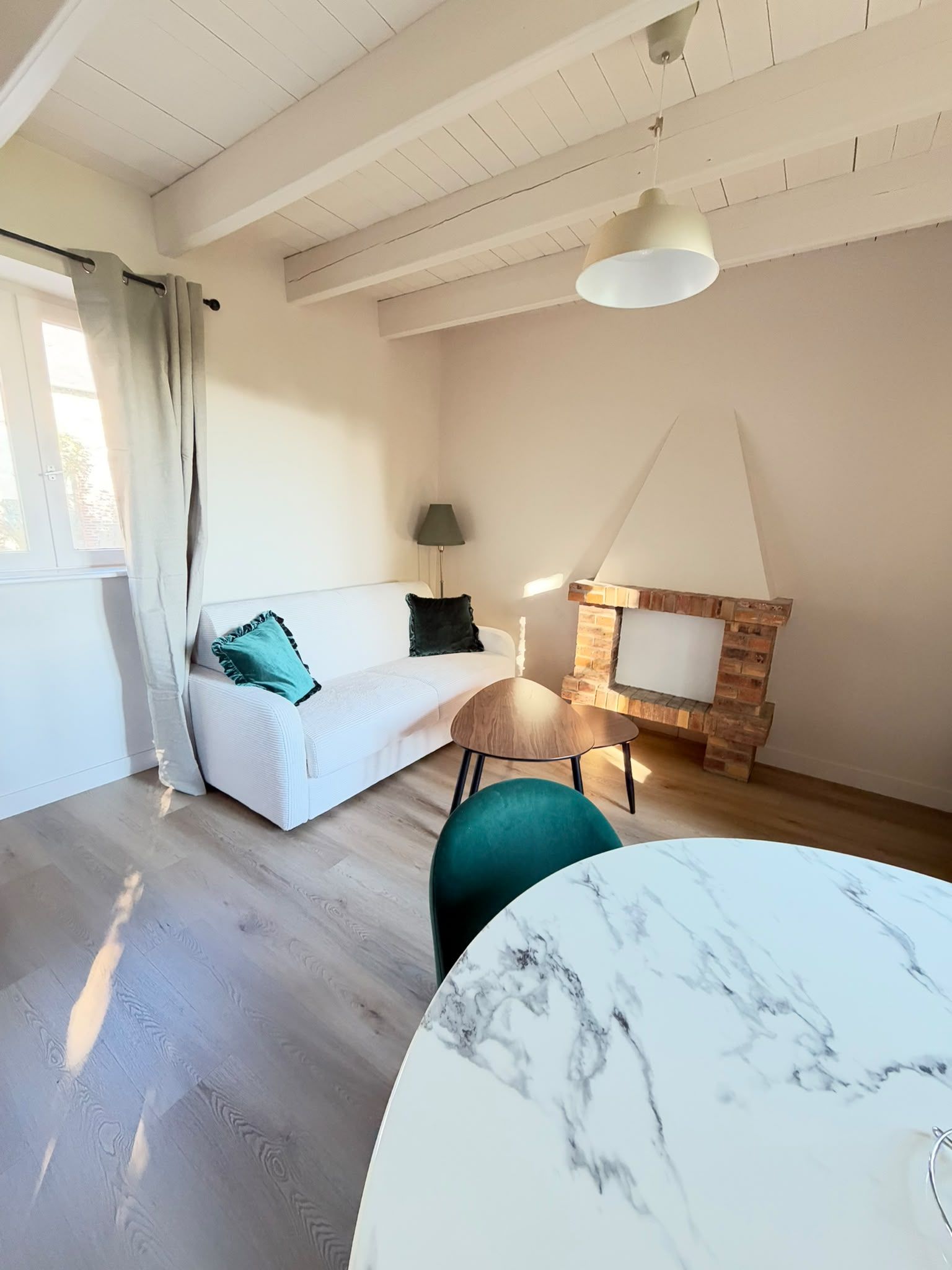 Uma sala de estar com sofá branco, mesa redonda de mármore, lareira de tijolo e ventilador de teto.