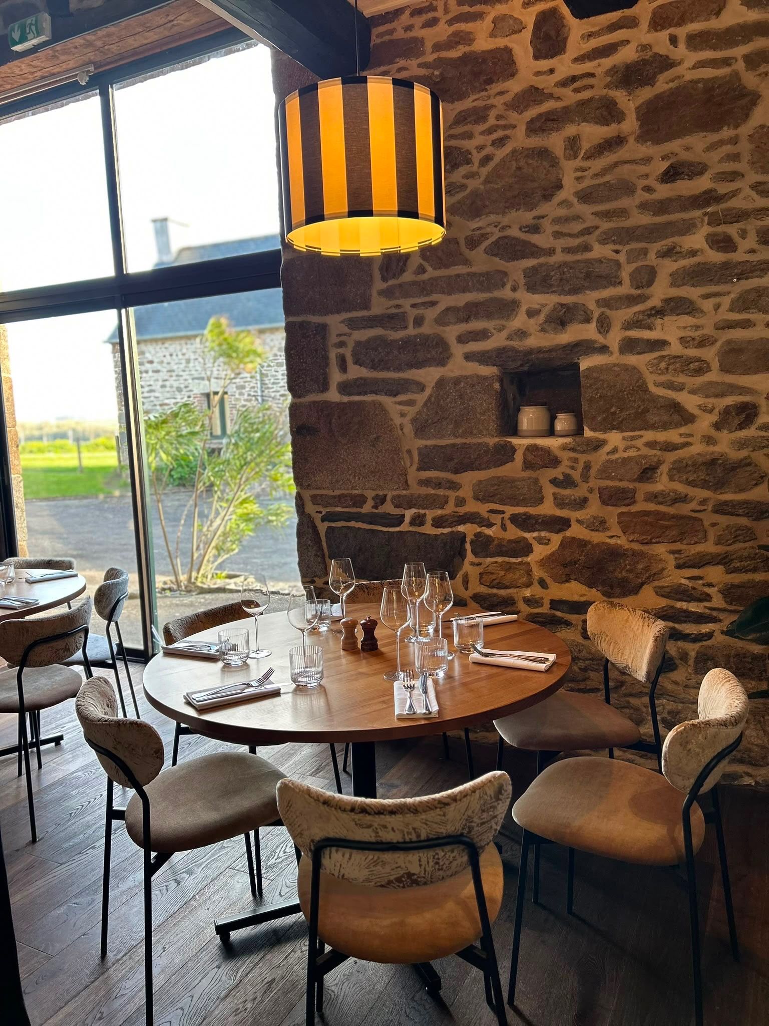 Een restaurantinterieur met een stenen muur, ronde tafels en stoelen.