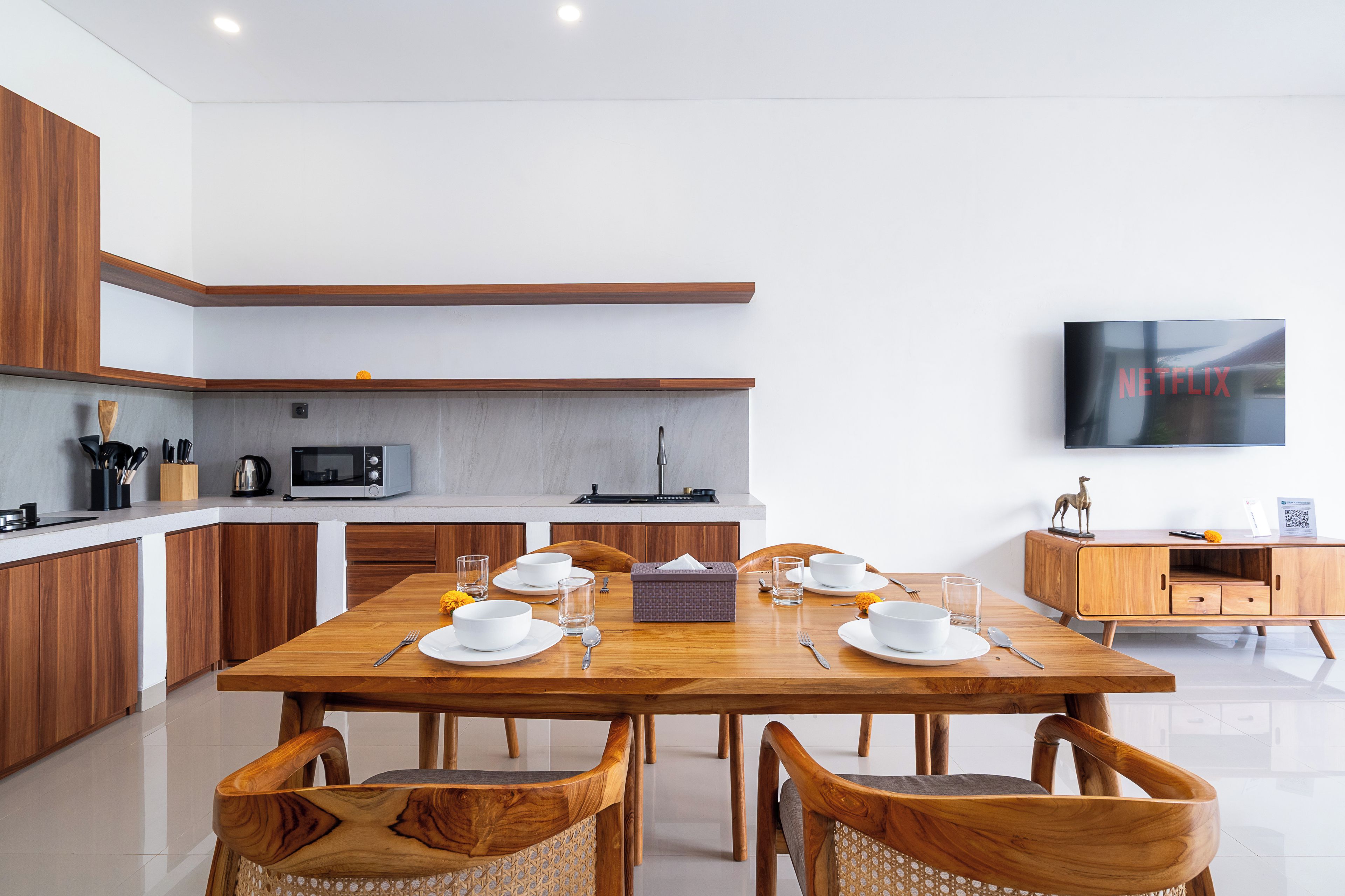 A modern kitchen with a dining area, wooden cabinets, a microwave, and a flat-screen TV.