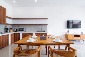 A modern kitchen with a dining area, wooden cabinets, a microwave, and a flat-screen TV. - VILLA LITAN SEMINYAK  (Kec Kuta)