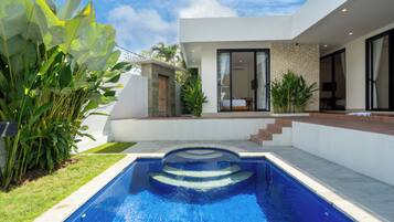 A modern house with a swimming pool, a stone wall, and a wooden door.