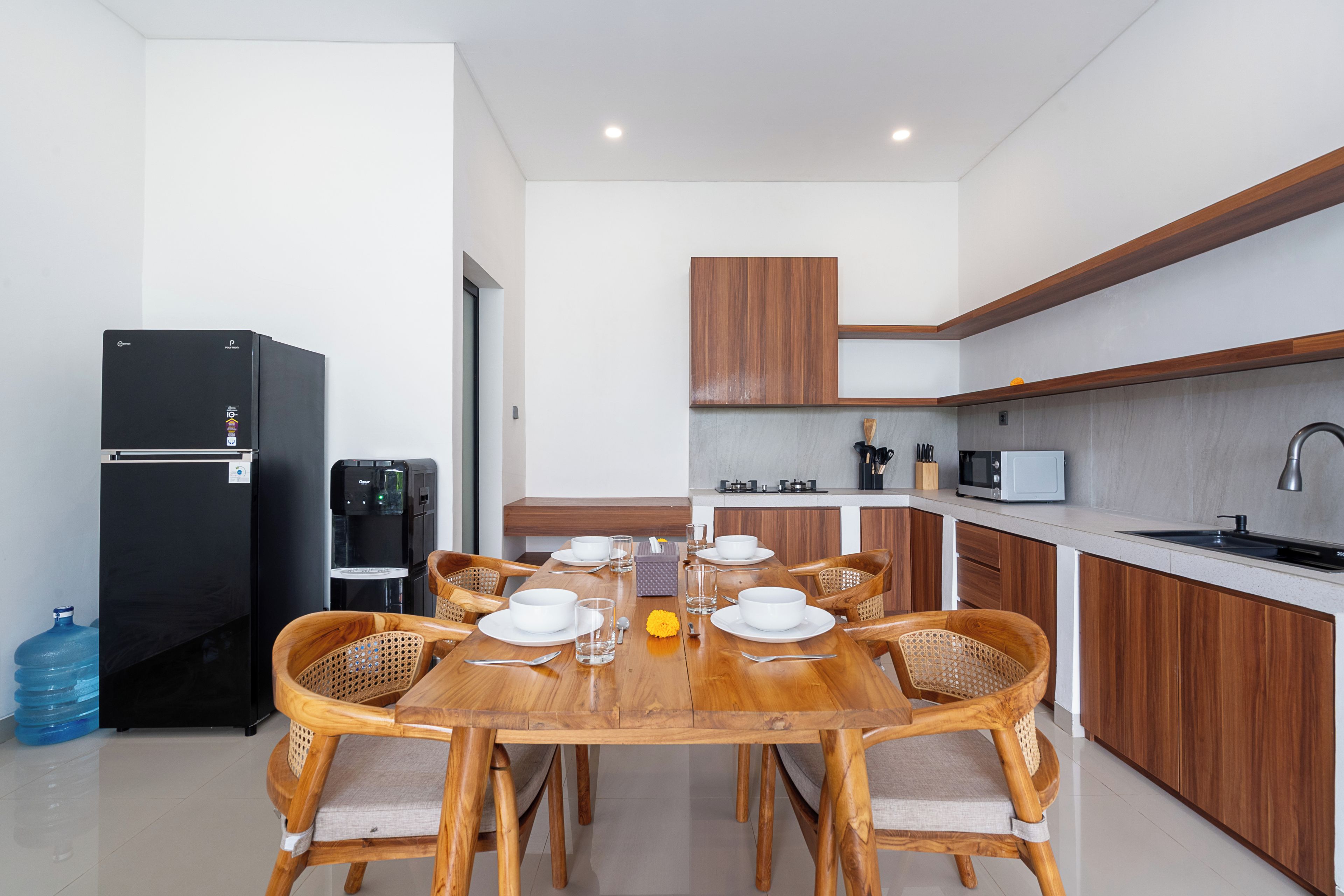 A modern kitchen with a dining area, equipped with a refrigerator, water dispenser, microwave, and a sink.