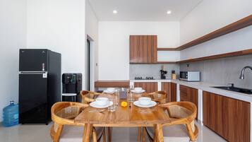 A modern kitchen with a dining area, equipped with a refrigerator, water dispenser, microwave, and a sink.