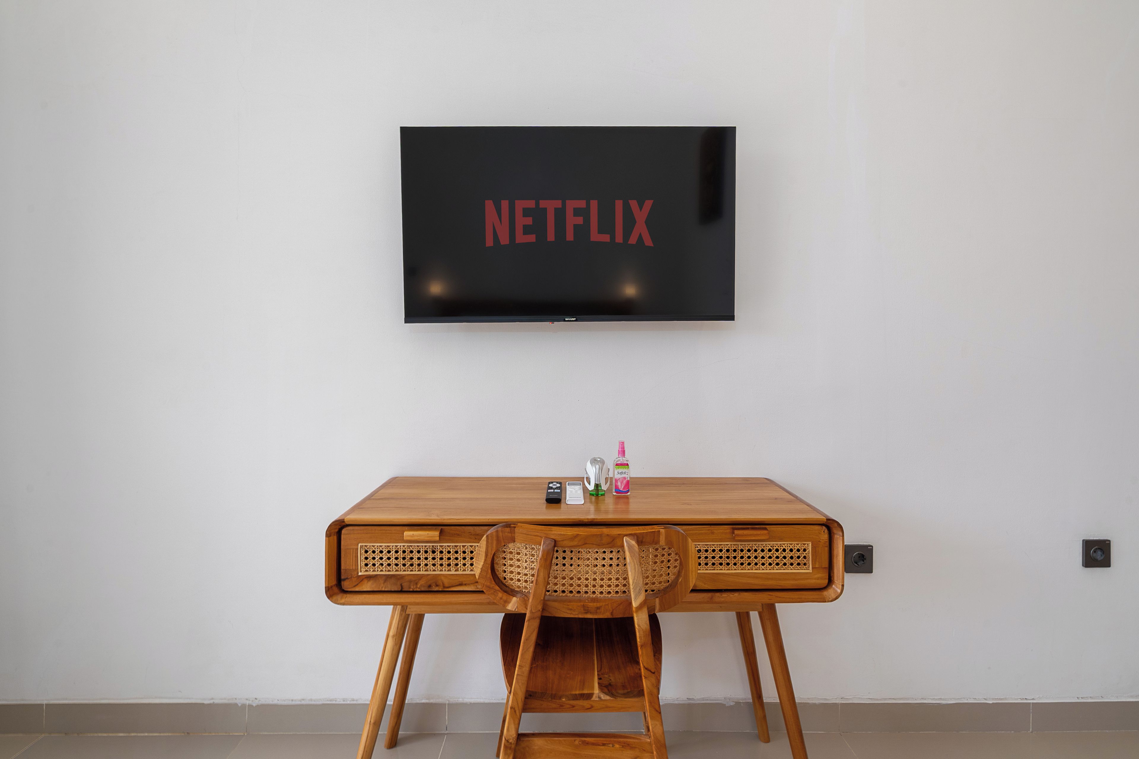 A room with a wooden table, a television mounted on the wall displaying 'NETFLIX', and a chair in front.