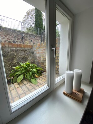 A room with a window overlooking a brick wall and a small garden area with plants. - Vrbo Property (Buckow (Märkische Schweiz))
