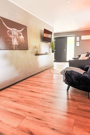 A modern living room with a wooden floor, a mounted TV, a dark sofa, and a large painting on the wall. - Seite Deern by Interhome (Altwarp)