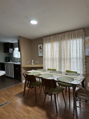 A dining area with a table set for four, surrounded by chairs, a kitchen in the background, and a window with curtains. - Comfortable Stay Near Downtown Austin/ The Domain (Austin)
