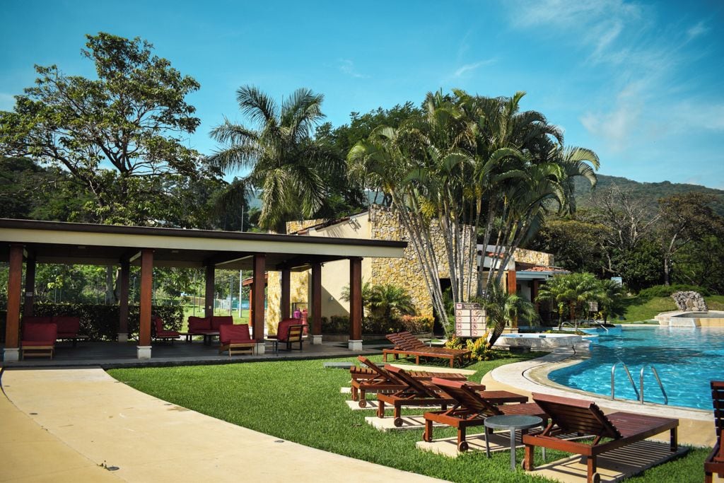 A pool area with lounge chairs, a covered seating area, and a stone building.