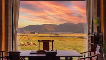 A dining area with a table and chairs, a view of a field with sheep, and mountains in the distance.