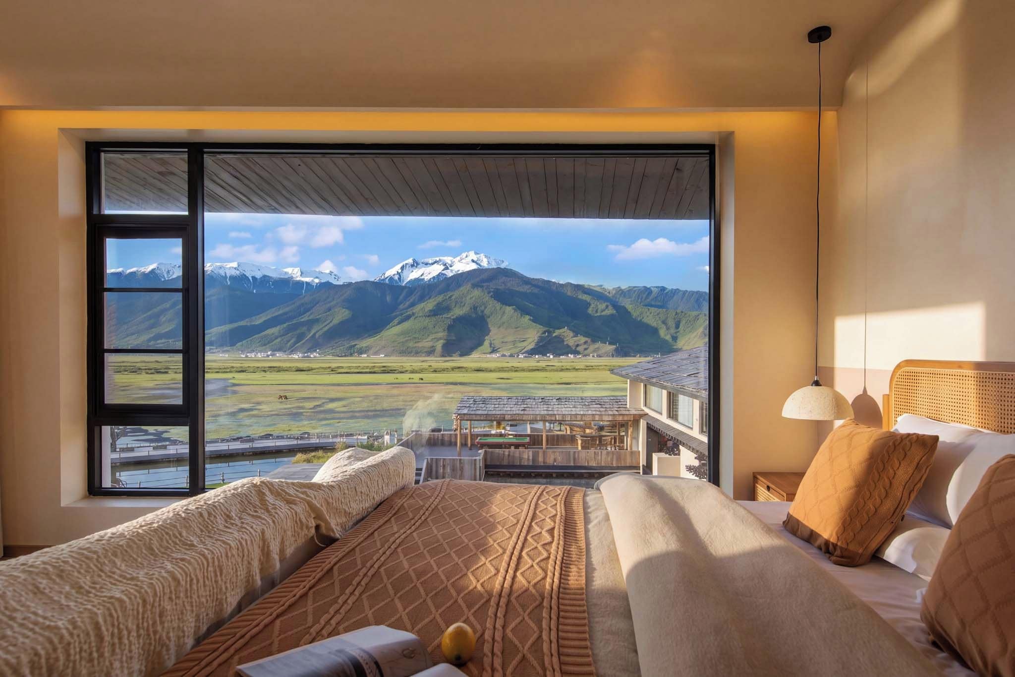 A bedroom with a large window offering a mountain view, a bed with patterned bedding, and a wooden ceiling.
