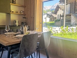 A dining area with a wooden table set for two, a coffee machine, and a view of traditional houses through a large window. - The Stalluccia by Interhome (Stampa)