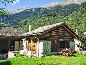 A rustic mountain cabin with a stone chimney, wooden exterior, and a dining area with outdoor seating. - The Stalluccia by Interhome (Stampa)