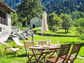 An outdoor dining area with a table set for four, surrounded by wooden chairs, in a lush green landscape with a mountain backdrop. - The Stalluccia by Interhome (Stampa)