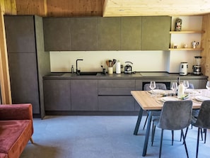 A modern kitchen with a central island, dark cabinetry, and a dining area with a table set for two. - The Stalluccia by Interhome (Stampa)