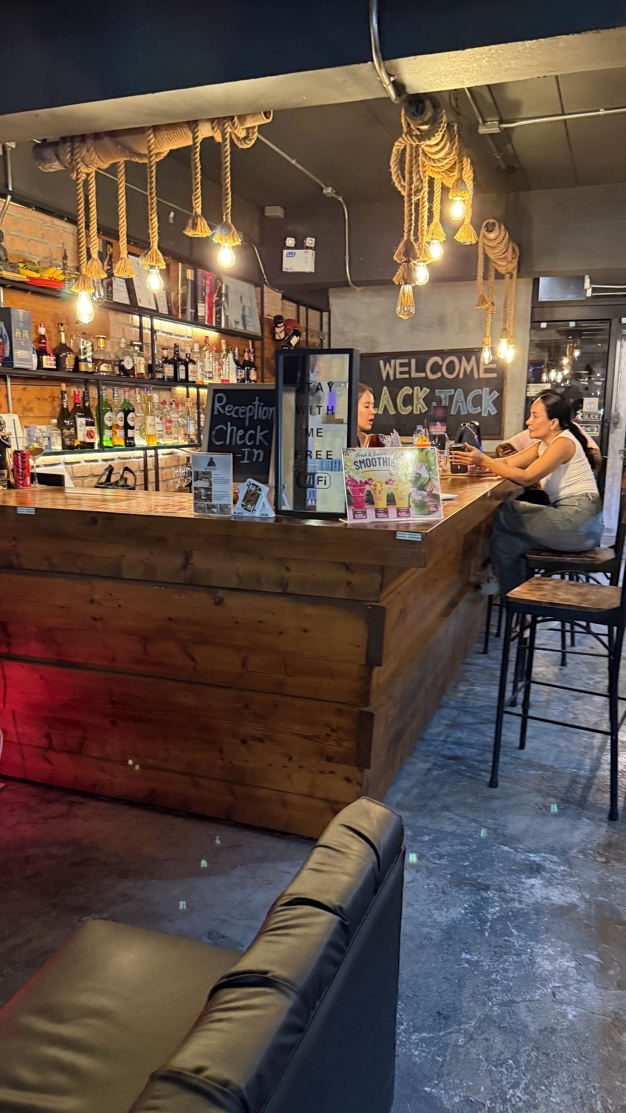 A bar area with a reception desk, wooden counter, and hanging light fixtures.