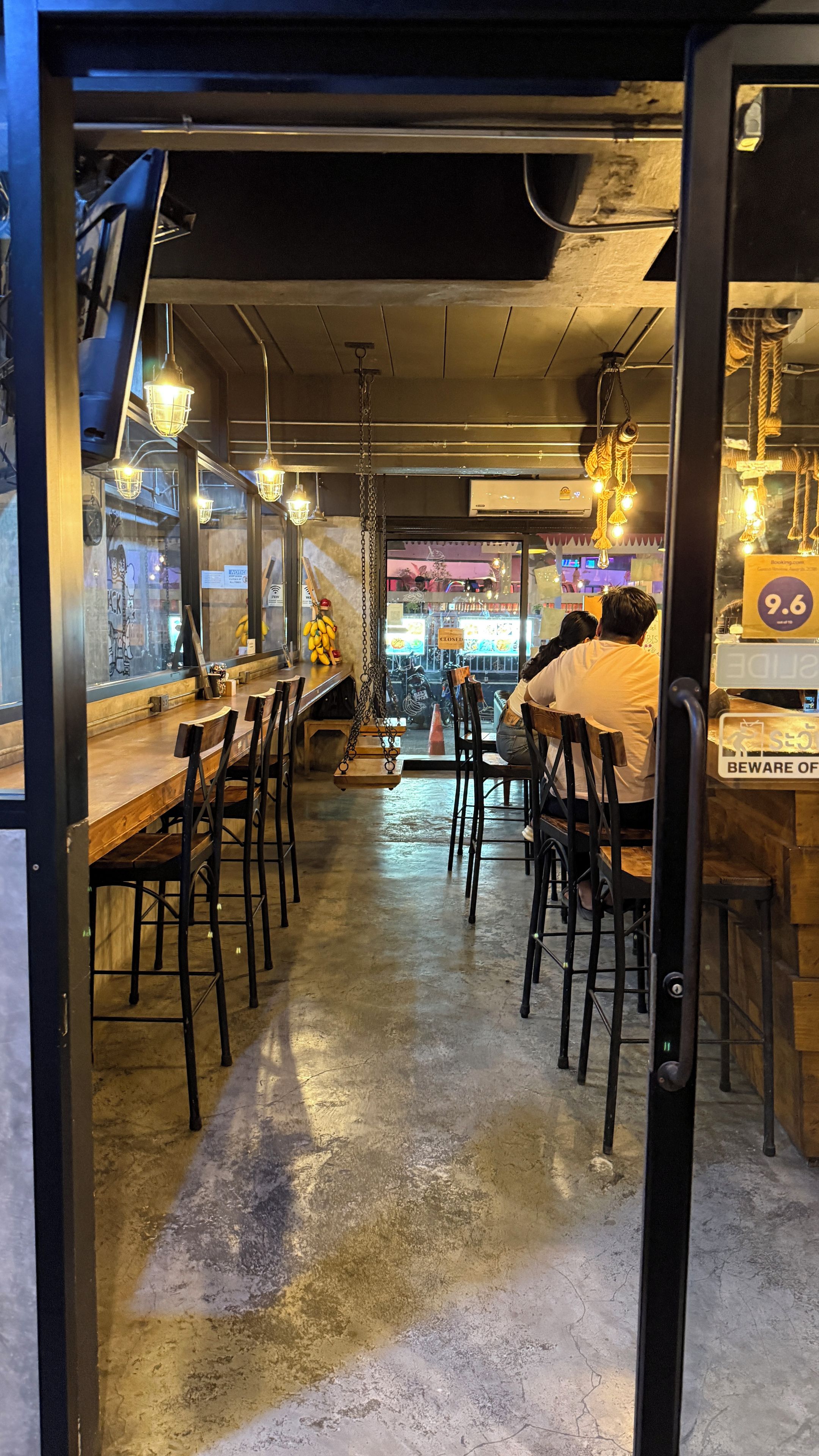 A restaurant interior with a long counter, bar stools, hanging light fixtures, and a closed sign.