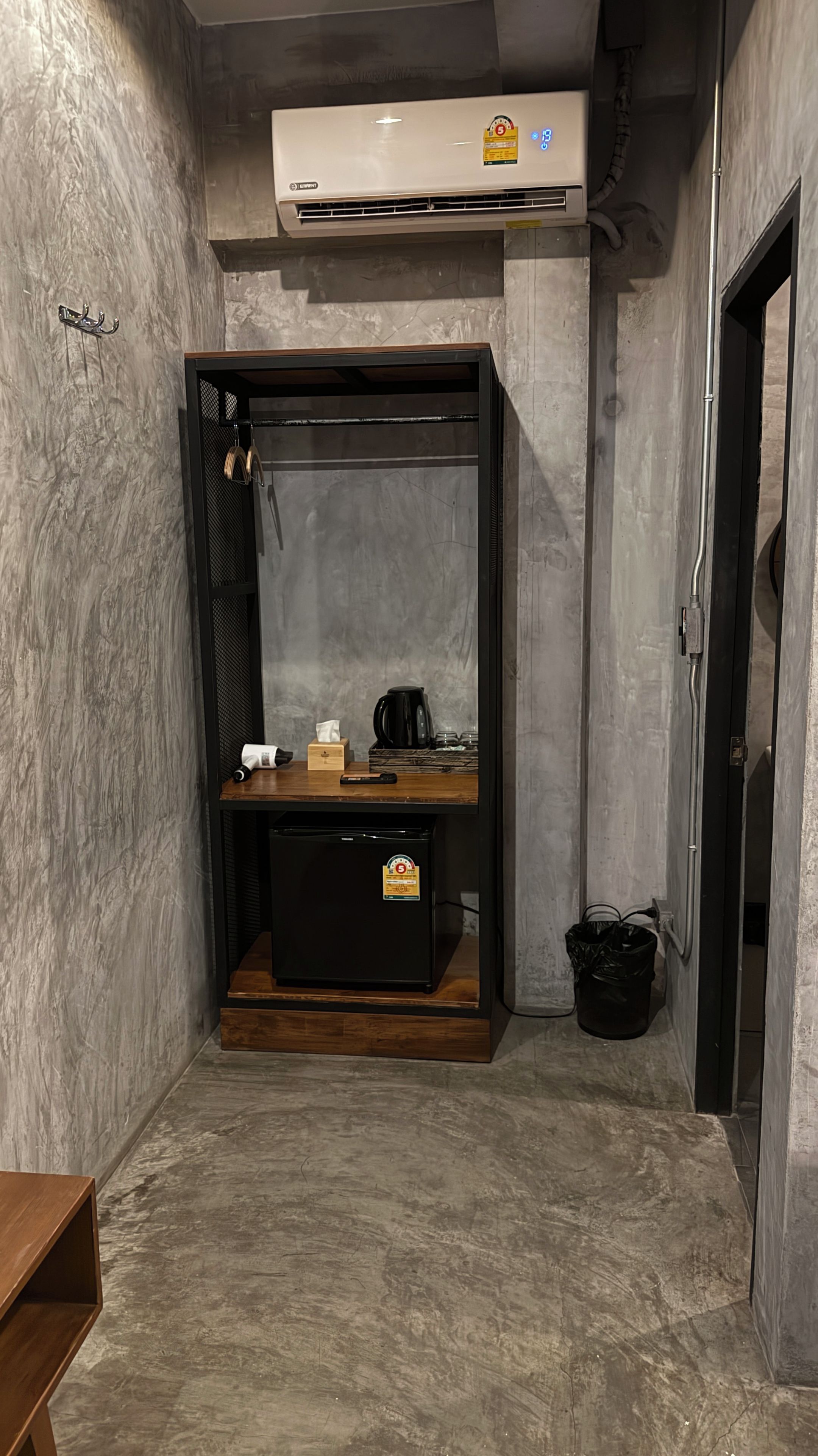 Una habitación compacta con aire acondicionado integrado, una pequeña mesa de madera con una tetera y un cesto de basura.