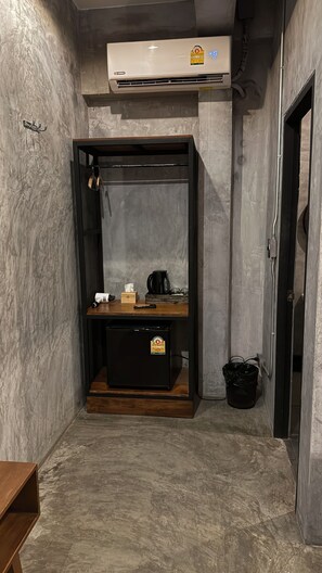 A compact room with a built-in air conditioning unit, a small wooden table with a kettle, and a trash bin. - Blackjack Bar and Hostel (Koh Samui)