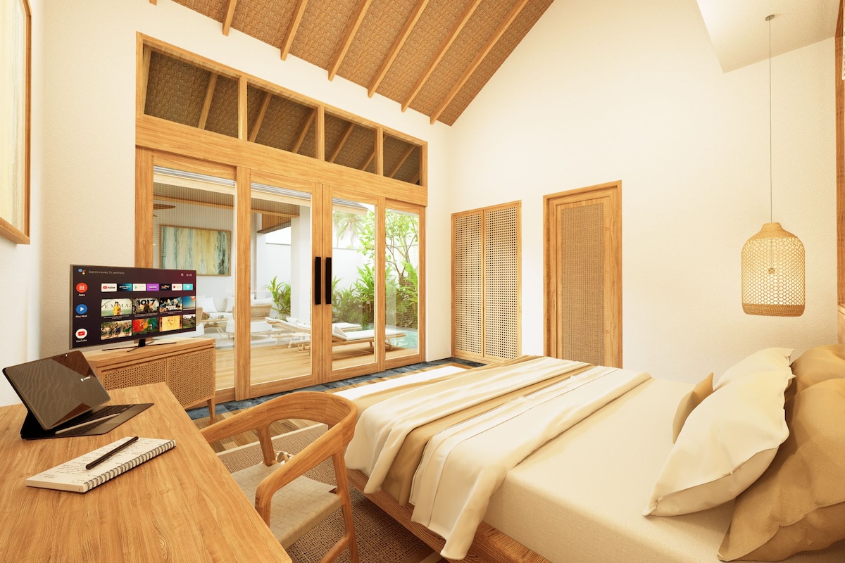 A bedroom with a bed, a desk with a laptop, a notebook, and a chair. There is a large window with a view of the outdoors.