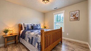 A bedroom with a wooden bed, a bedside table with a lamp, a window with blinds, and a wall-mounted painting. - Scenic Mountain Escape, Relax, Unwind & Explore (Boise)