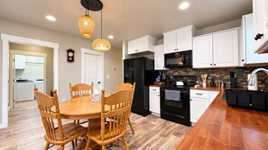 A modern kitchen with white cabinetry, a black refrigerator, and a wooden dining table with chairs. - Scenic Mountain Escape, Relax, Unwind & Explore (Boise)