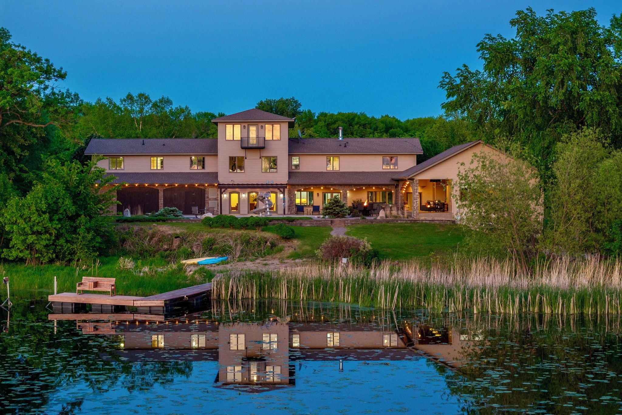 A large, multi-story house with a covered patio and a dock extending into a lake.
