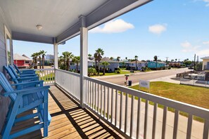 A covered porch with blue chairs, a stop sign, and a sign for 'Jaspon's Limousine' on a street with houses and palm trees. - Fluorescent Beauty 4BR Home (Port Aransas)