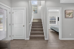 A staircase leading to a bedroom with a bed, a door, and a window with blinds. - Fluorescent Beauty 4BR Home (Port Aransas)