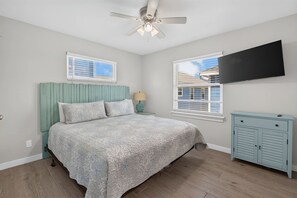 A bedroom with a bed, a ceiling fan, a television, and a window. - Fluorescent Beauty 4BR Home (Port Aransas)