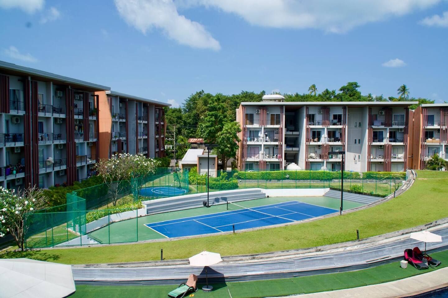 A residential building complex with multiple balconies, a tennis court, and a landscaped garden area.