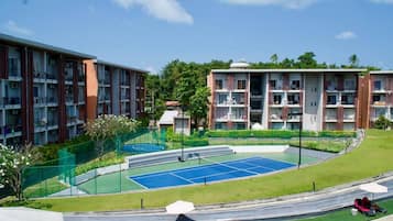A residential building complex with multiple balconies, a tennis court, and a landscaped garden area.