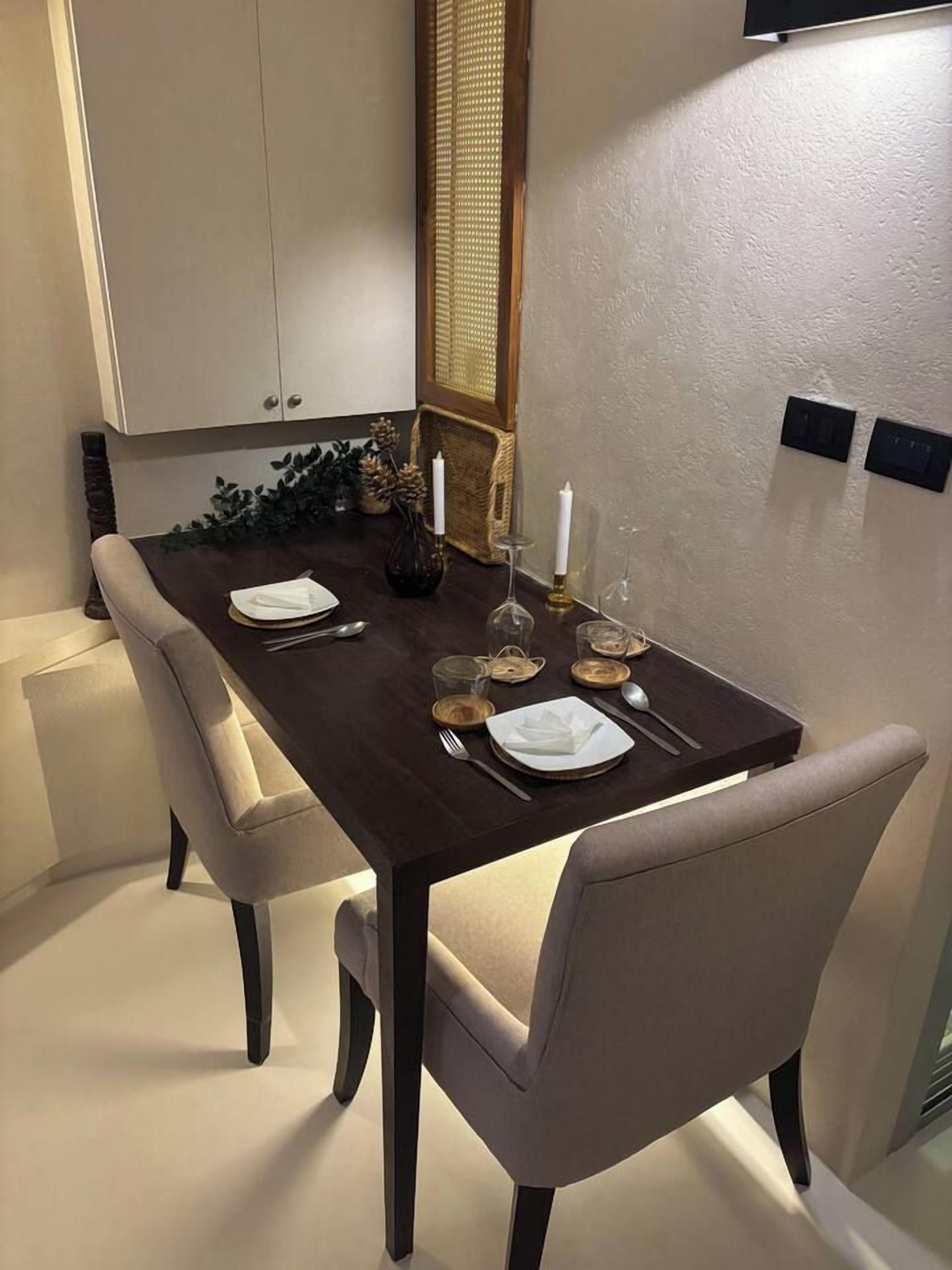 Un coin repas avec une table en bois foncé, dressée pour quatre personnes, des chaises à revêtement beige et un meuble blanc placé au-dessus.