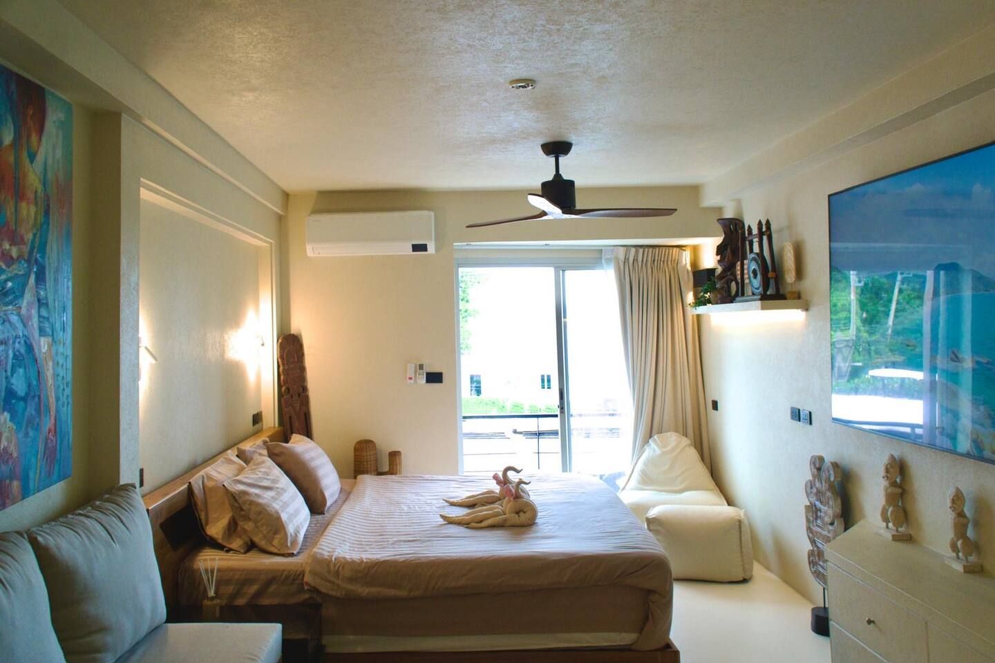 A hotel room with a bed, a sofa, a ceiling fan, and a large window.