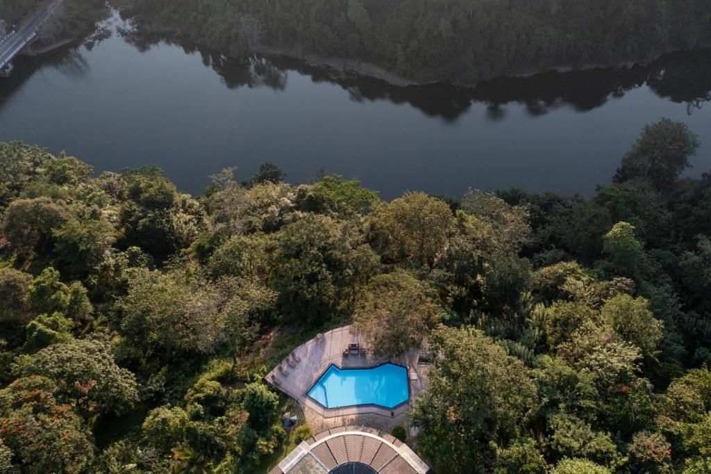 Vista aérea de una propiedad con piscina rodeada de bosque frondoso, un puente al fondo y un reflejo claro en el agua.