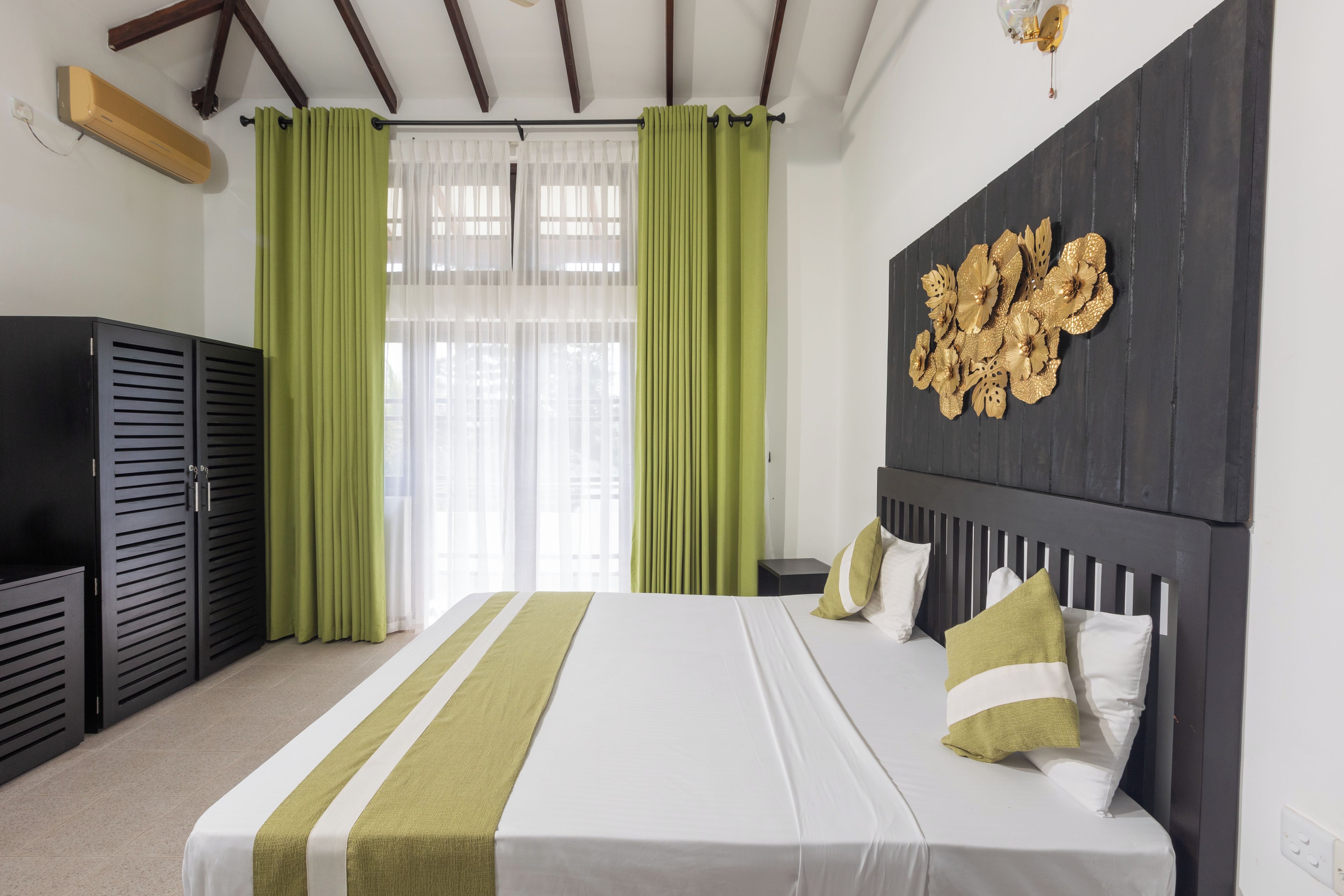 Une chambre d’hôtel avec un lit, des rideaux verts, un élément décoratif mural et un plafond en bois.
