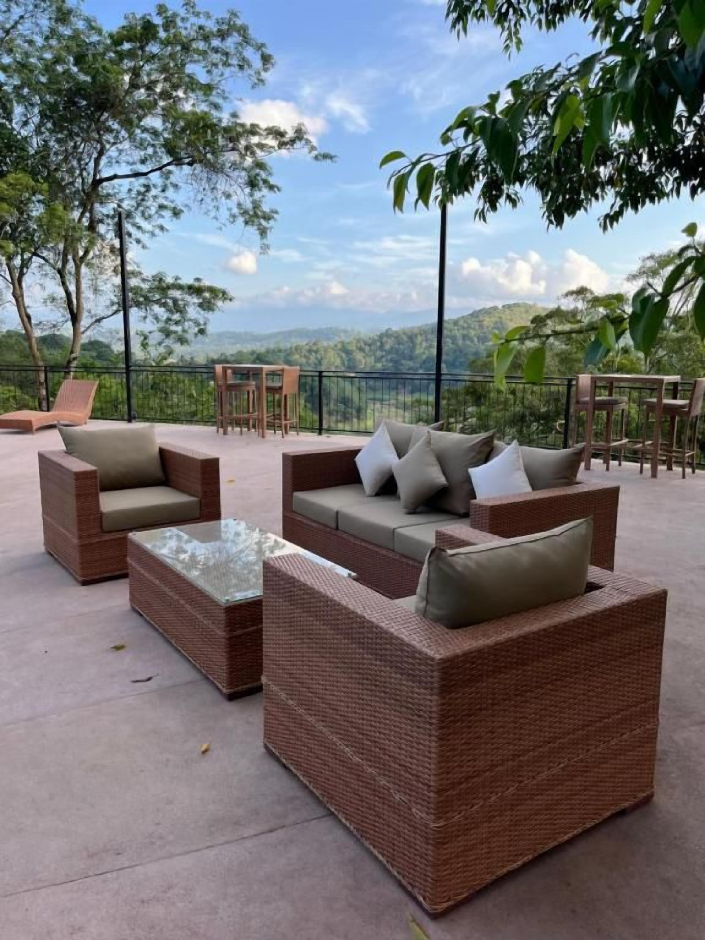 Mobilier d’extérieur en osier, agrémenté de coussins, avec une table à plateau en verre et une vue sur un paysage montagneux.