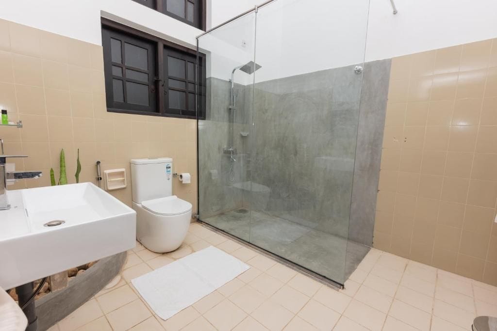 A bathroom with a glass-enclosed shower, a white sink, and a toilet.