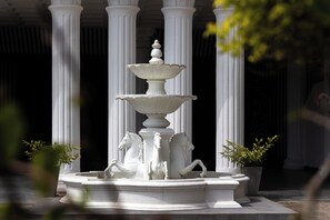 A white stone fountain with multiple tiers and horse statues, surrounded by white columns.