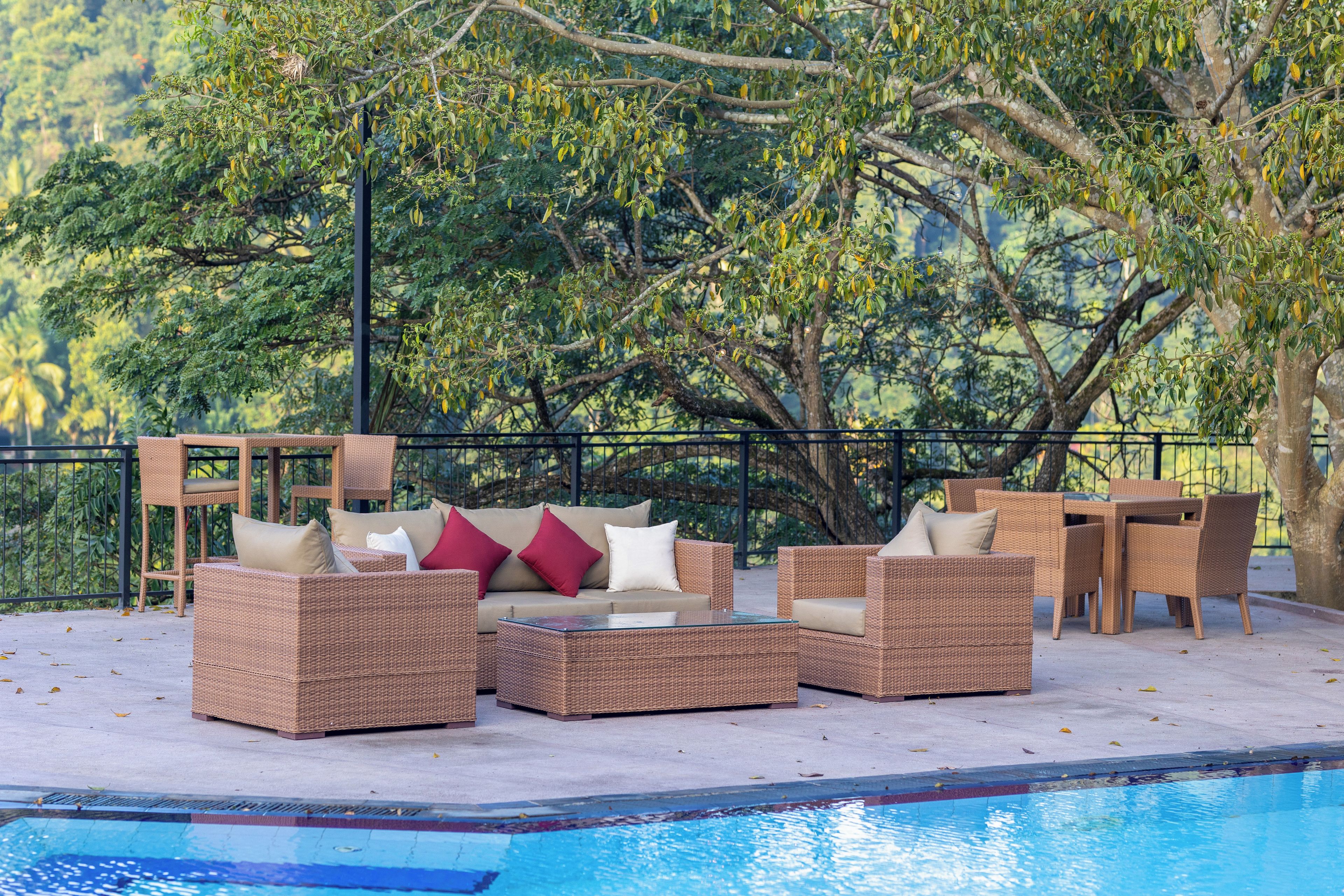 A poolside area with wicker furniture and a view of trees.
