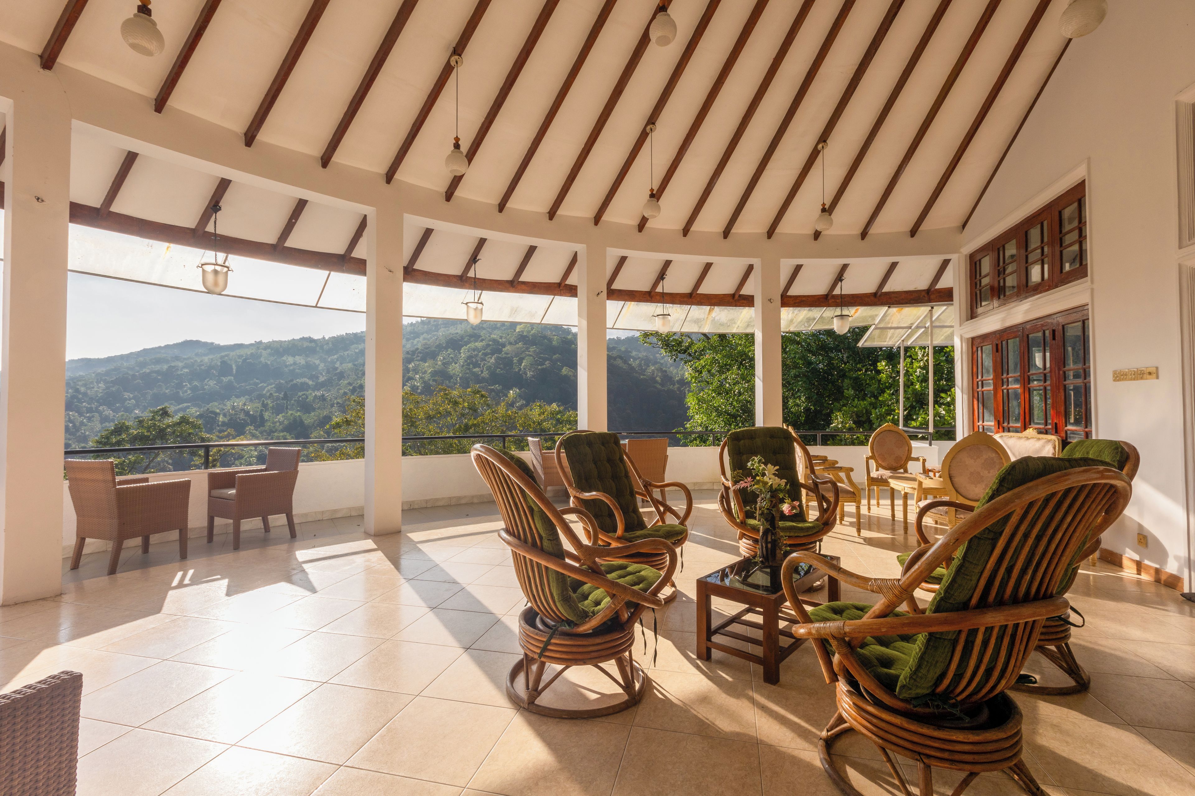 A covered outdoor seating area with wicker furniture, large windows, and a view of a mountainous landscape.