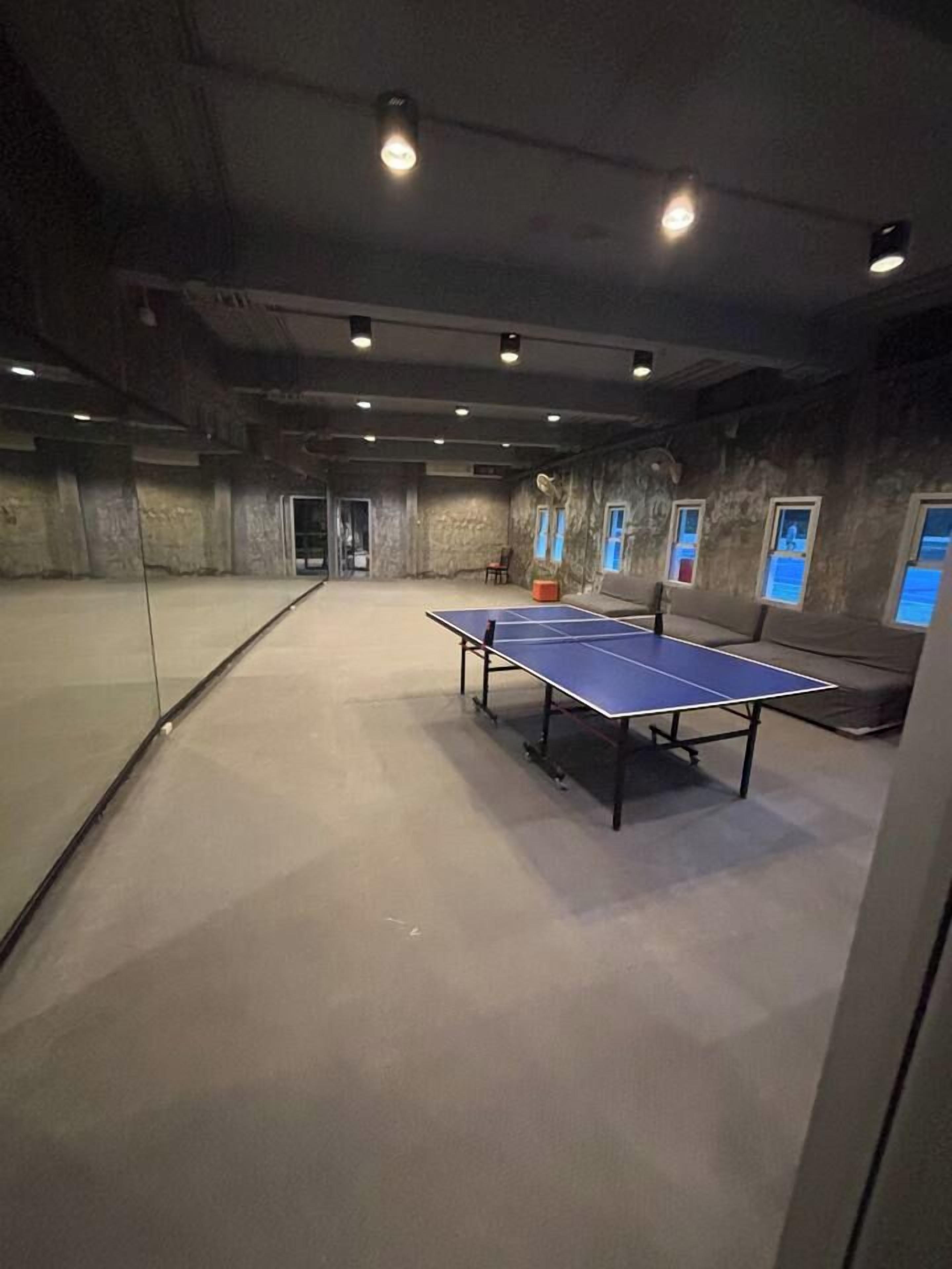 Une pièce avec une table de ping-pong, un canapé et une cloison en verre.