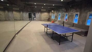 Une pièce avec une table de ping-pong, un canapé et une cloison en verre.
