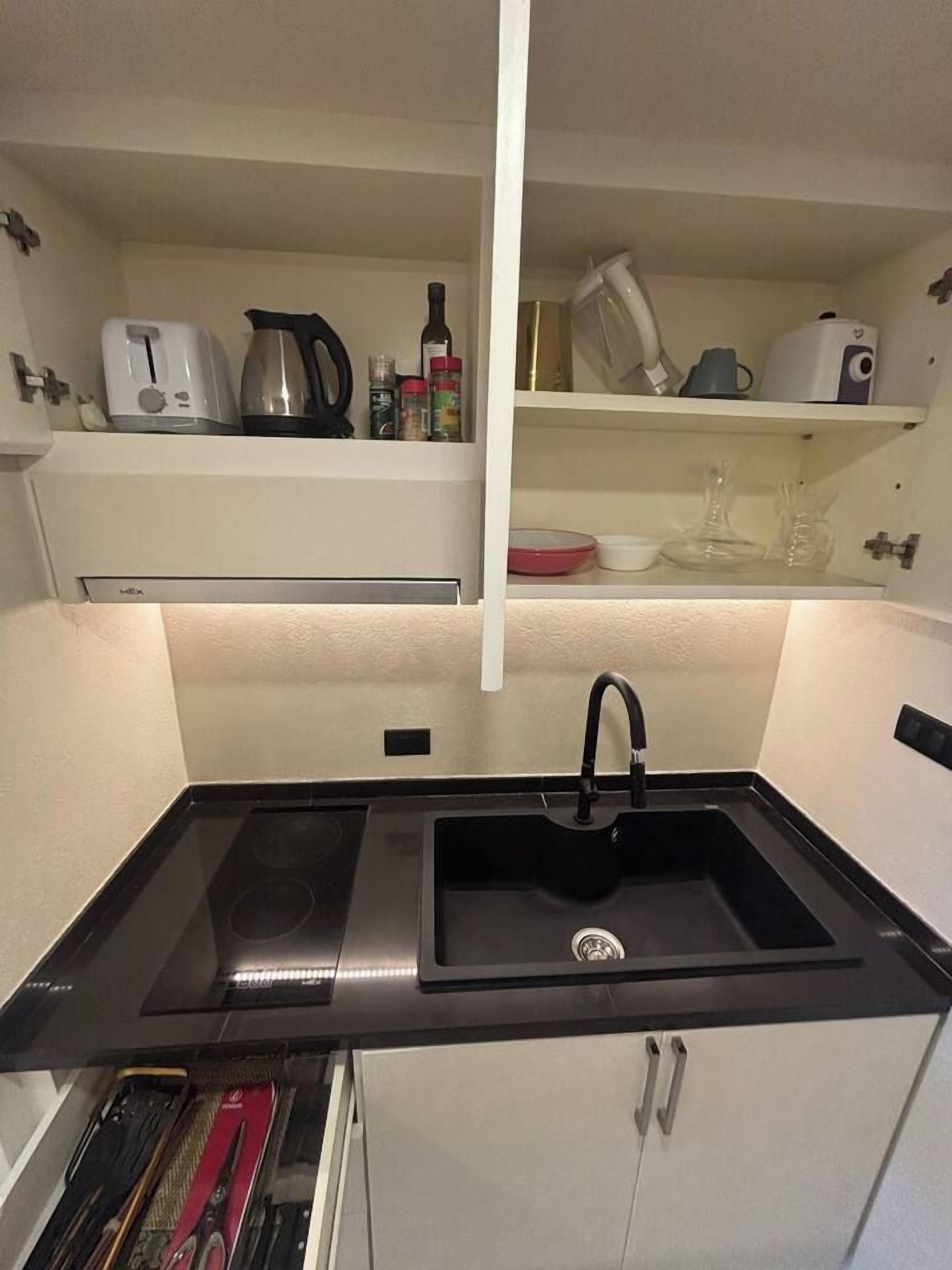 Une cuisine compacte avec un plan de travail noir, un évier et une cuisinière intégrée.