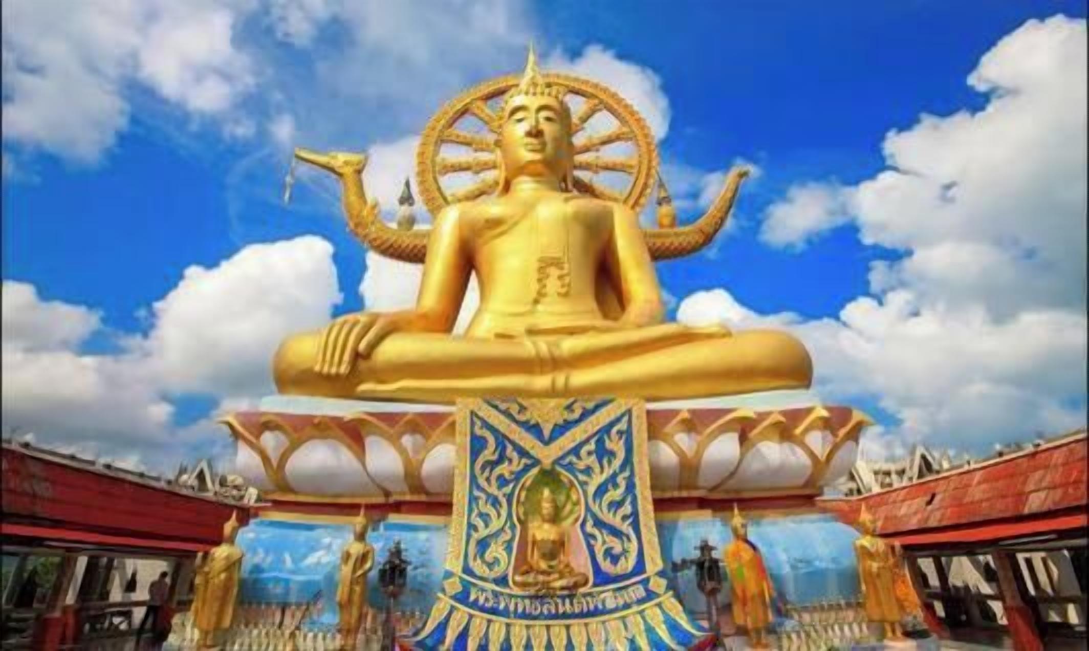 A large golden statue of a seated figure with multiple arms, set against a clear sky.