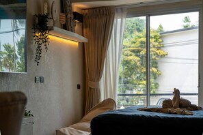 Une chambre à coucher avec un lit, une fenêtre avec des rideaux, un luminaire fixé au mur et une plante.