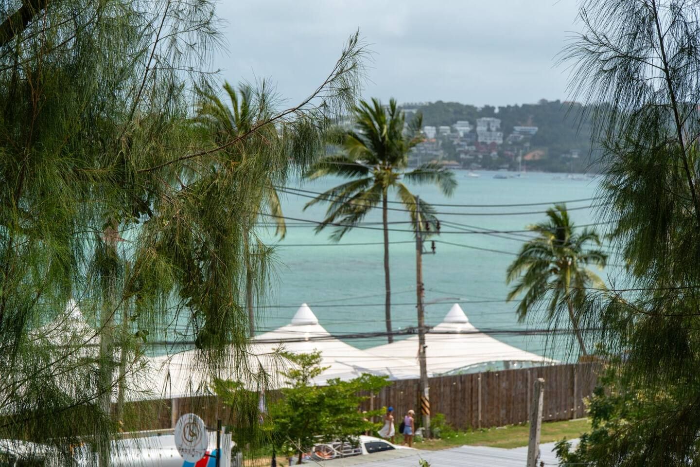 A view of a coastal area with a wooden fence, a white tent structure, and a body of water.