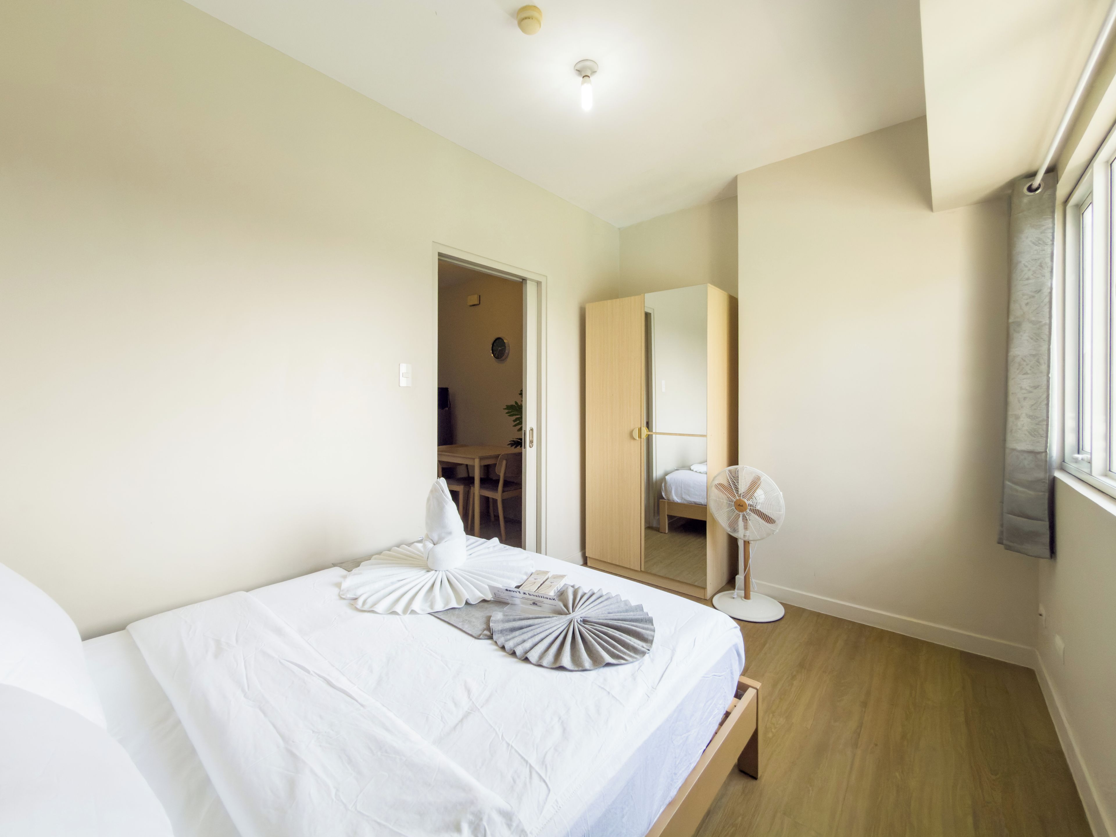 Un dormitorio con cama, mesita de noche y un ventilador de pie.