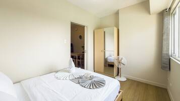 Un dormitorio con cama, mesita de noche y un ventilador de pie.